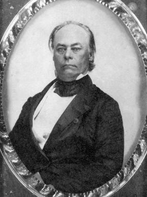 A formal, black-and-white portrait of a man in a coat and cravat, captured within an oval frame.