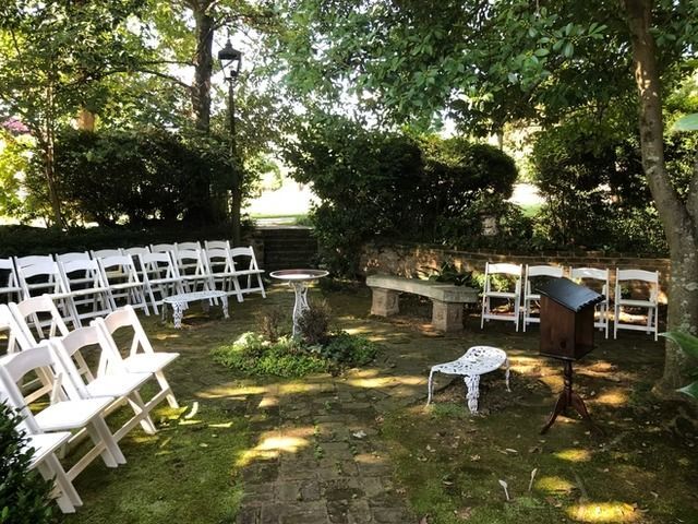 Outdoor wedding ceremony setup with white folding chairs arranged in rows on a stone patio surrounded by trees.