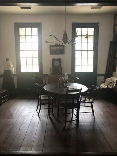 A round dining table and four chairs sit in a room with two tall windows, dark wood floors, and a hanging light fixture.