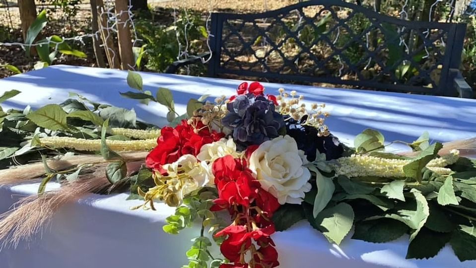 A floral arrangement with red, white, and dark blue flowers and greenery resting on a white table outdoors.