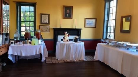A catered room with yellow walls and white-clothed tables, including a central table with a small statue and food warmers.