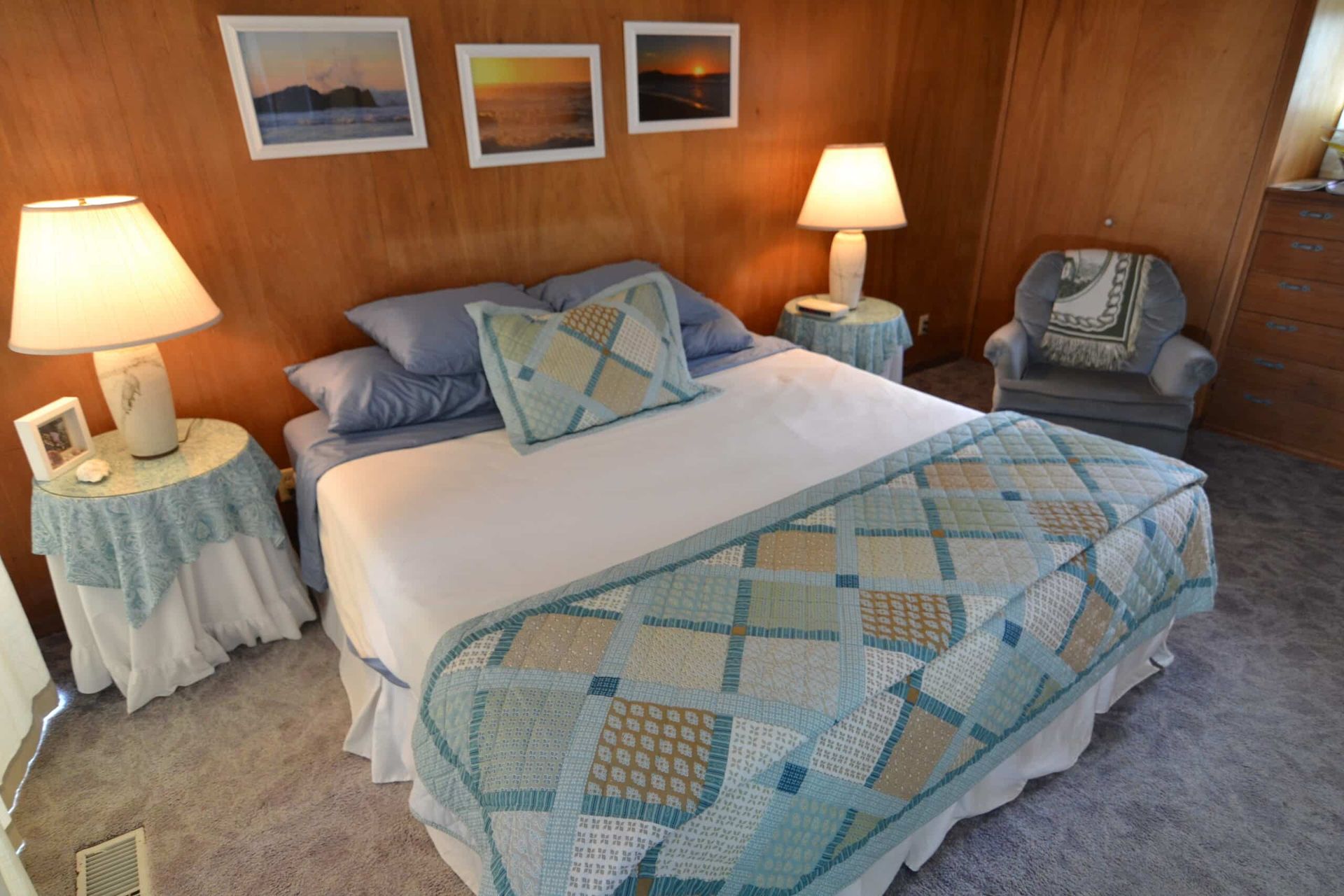 A bedroom with a bed , chair , lamps and pictures on the wall.