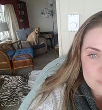 A woman is taking a selfie in a living room with a dog in the background.