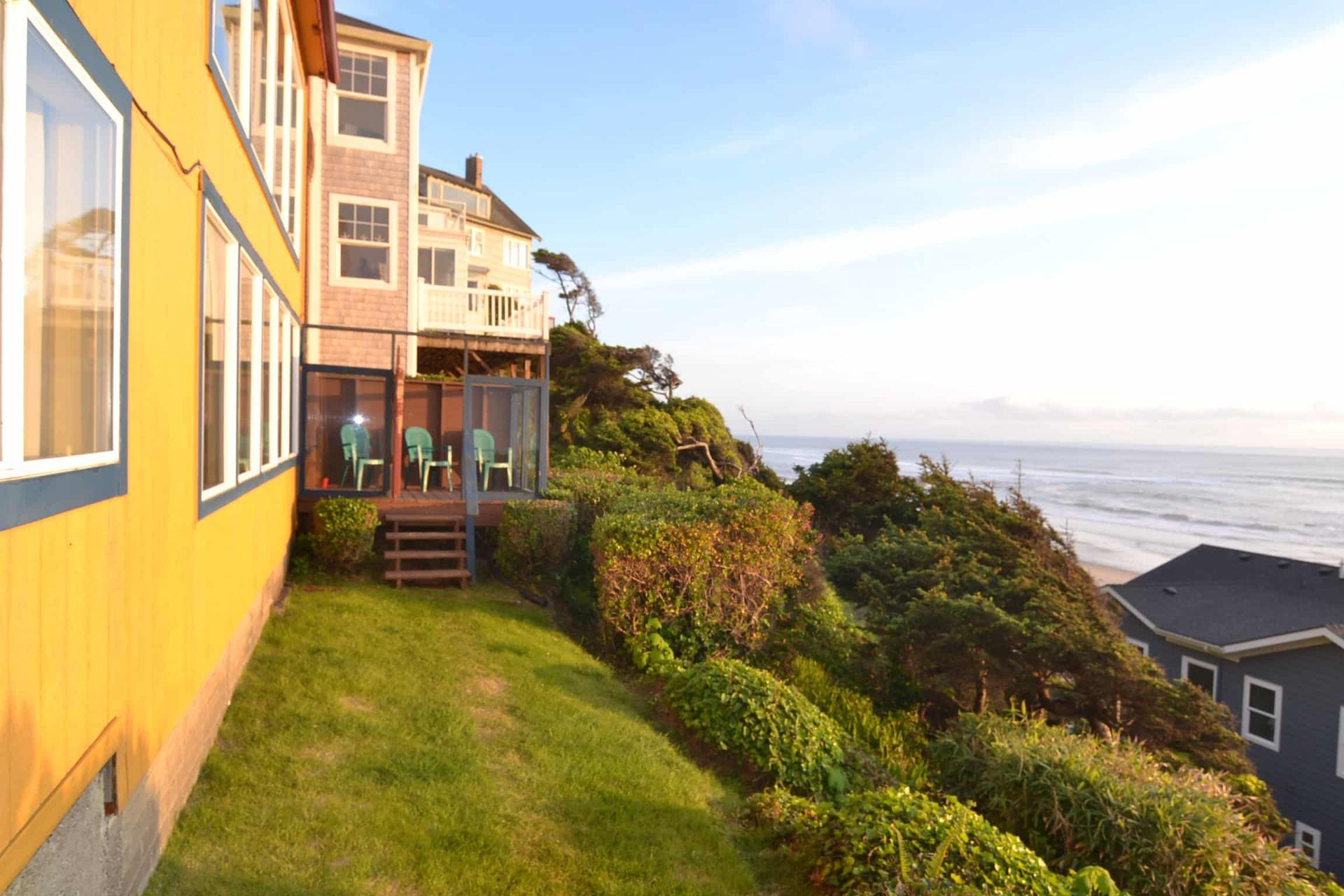 A yellow house sits on a hill overlooking the ocean