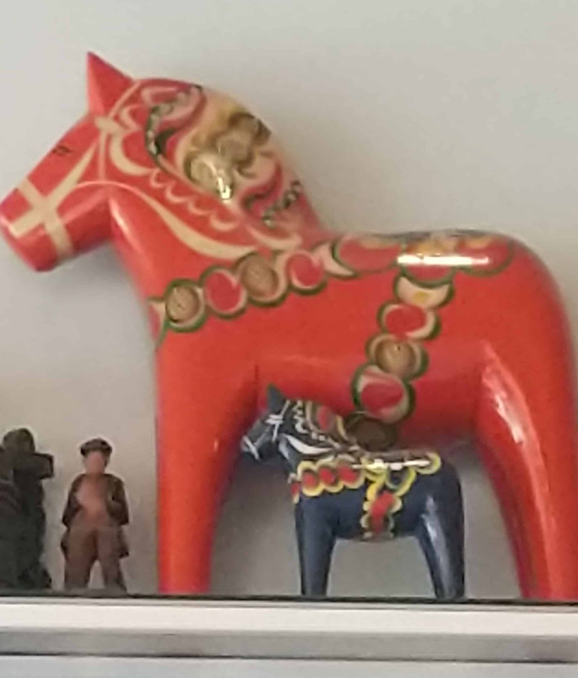 A red horse is standing next to a smaller horse on a shelf.