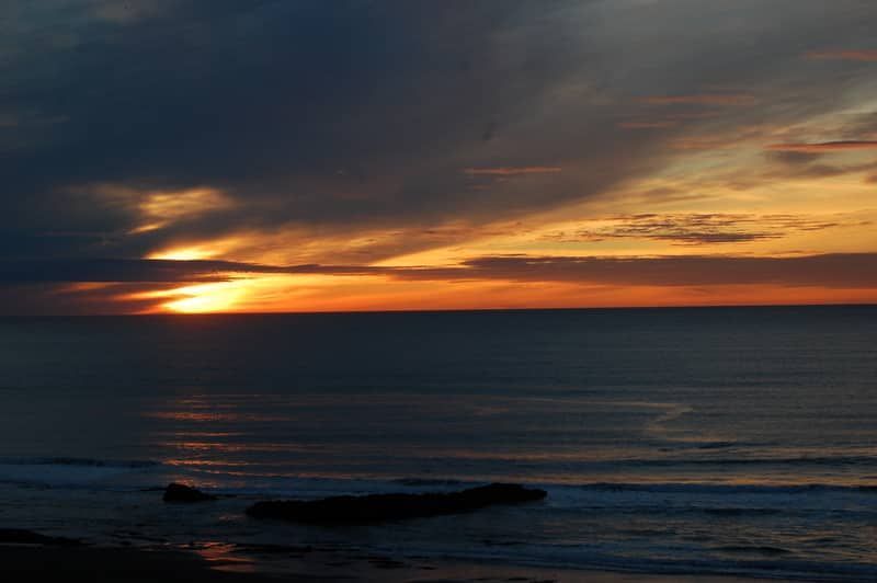 A sunset over the ocean with a rock in the foreground