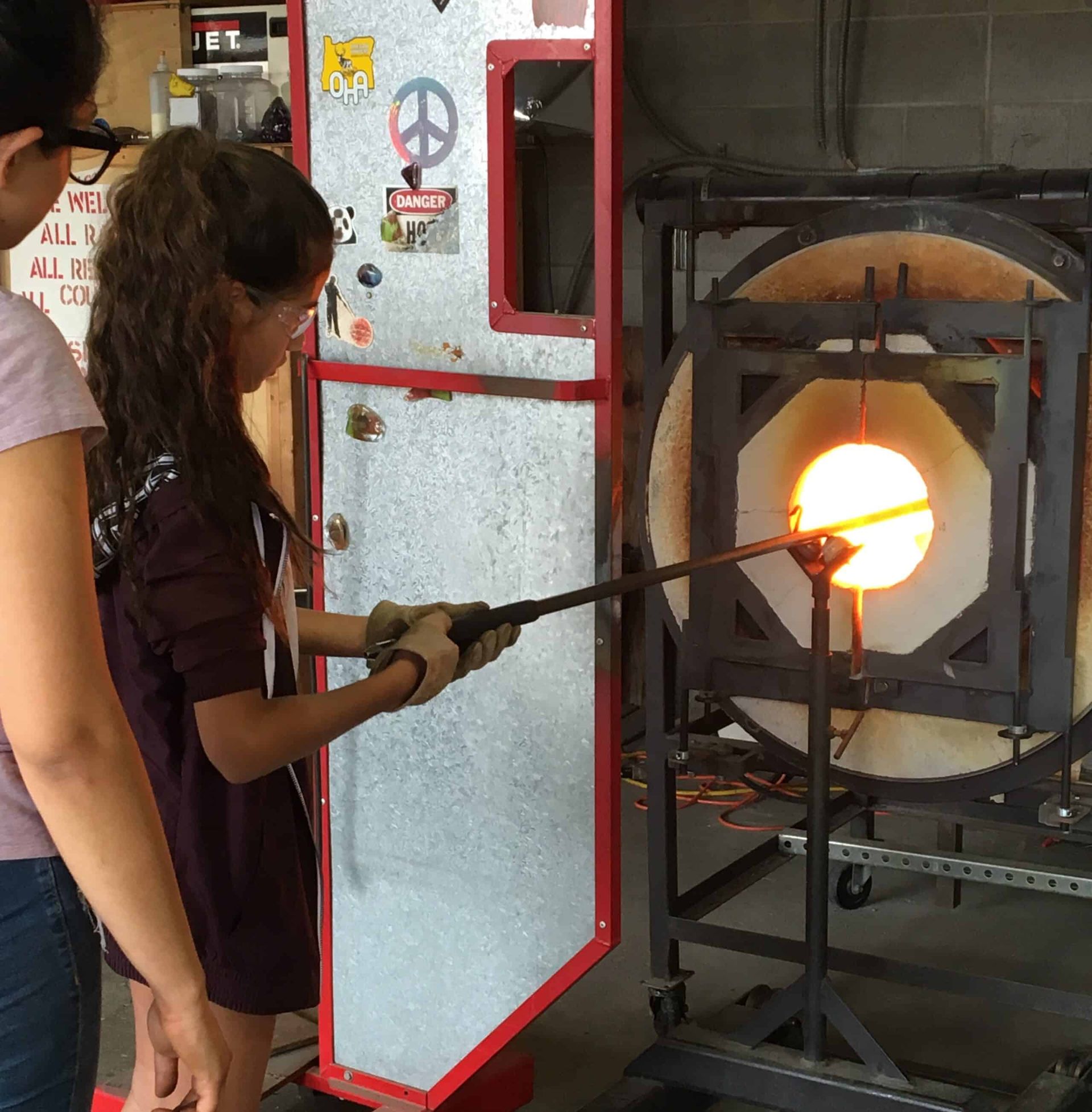 A woman holds a stick in front of a glass furnace