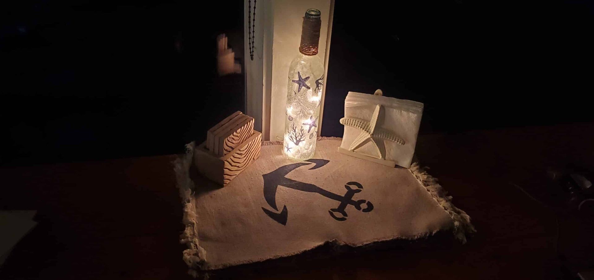 A pillow with an anchor on it is sitting on a wooden table.