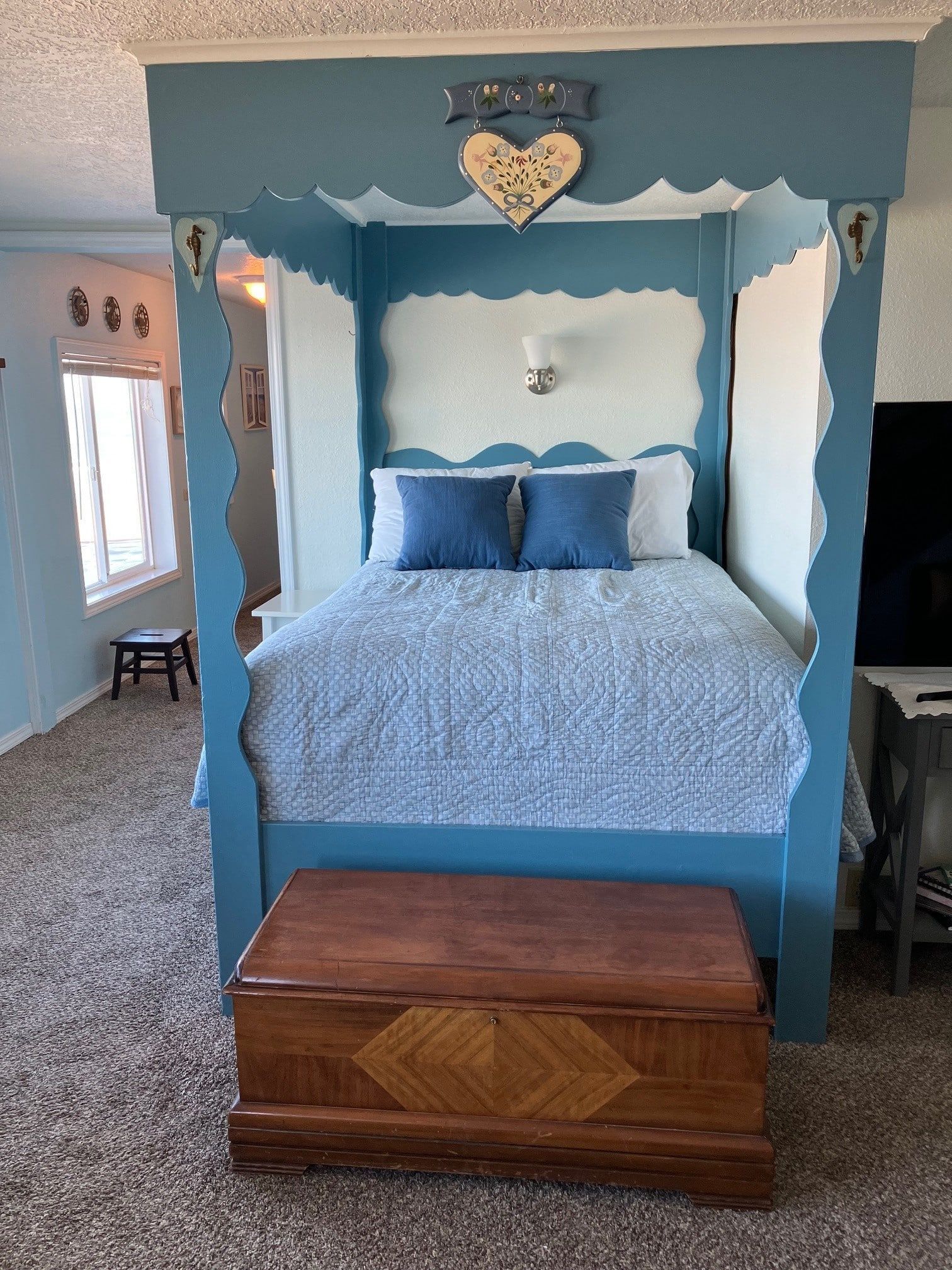 A blue canopy bed is in a bedroom next to a wooden trunk.