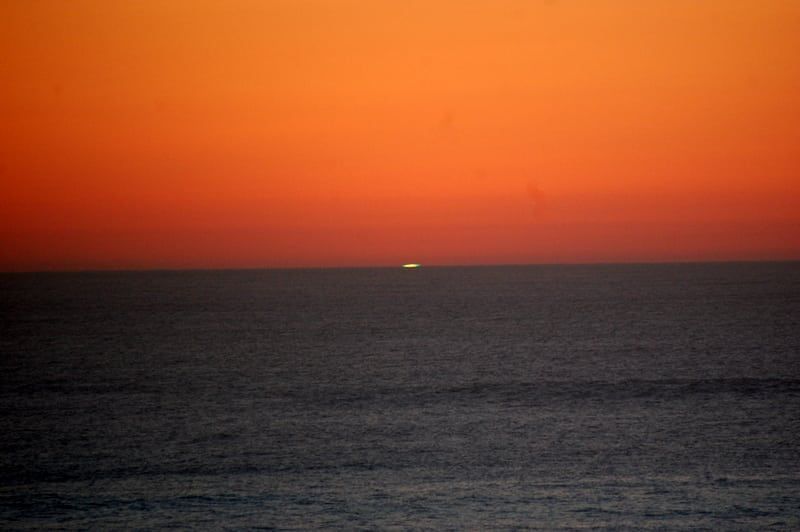 A sunset over the ocean with a boat in the distance.