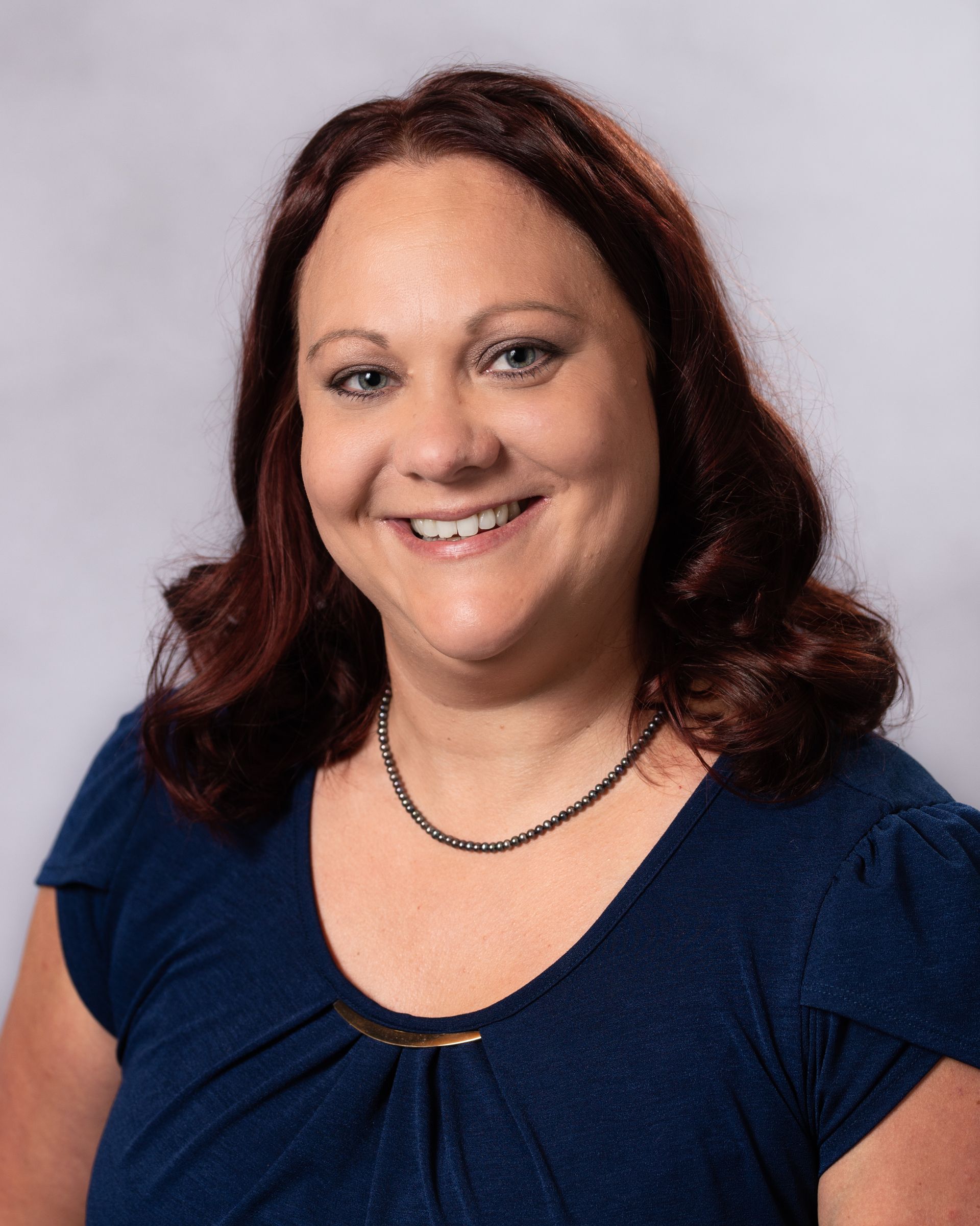 A woman wearing a blue shirt and a necklace is smiling for the camera.