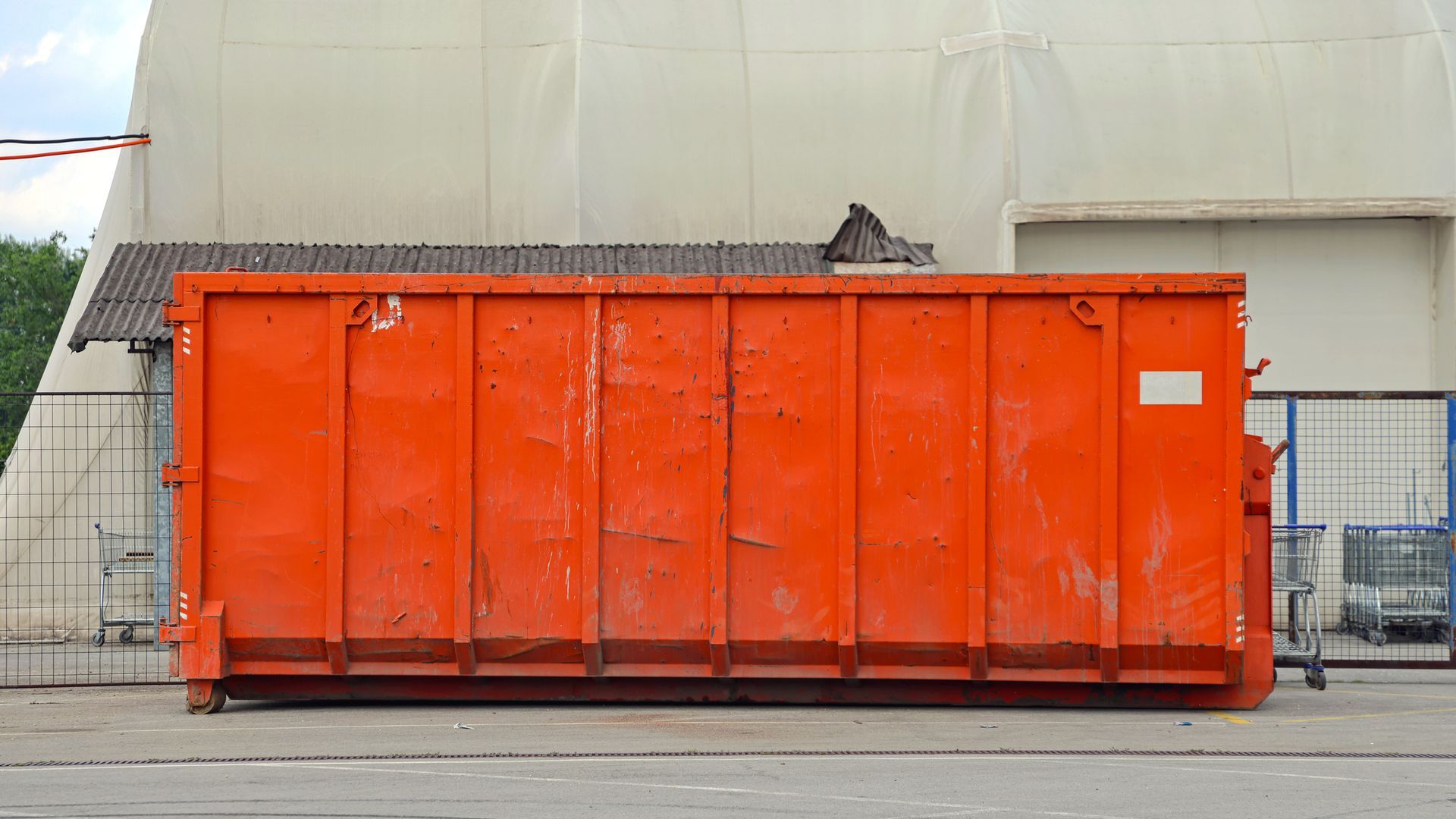 Orange dumpster in front of a tan building and gray ground.