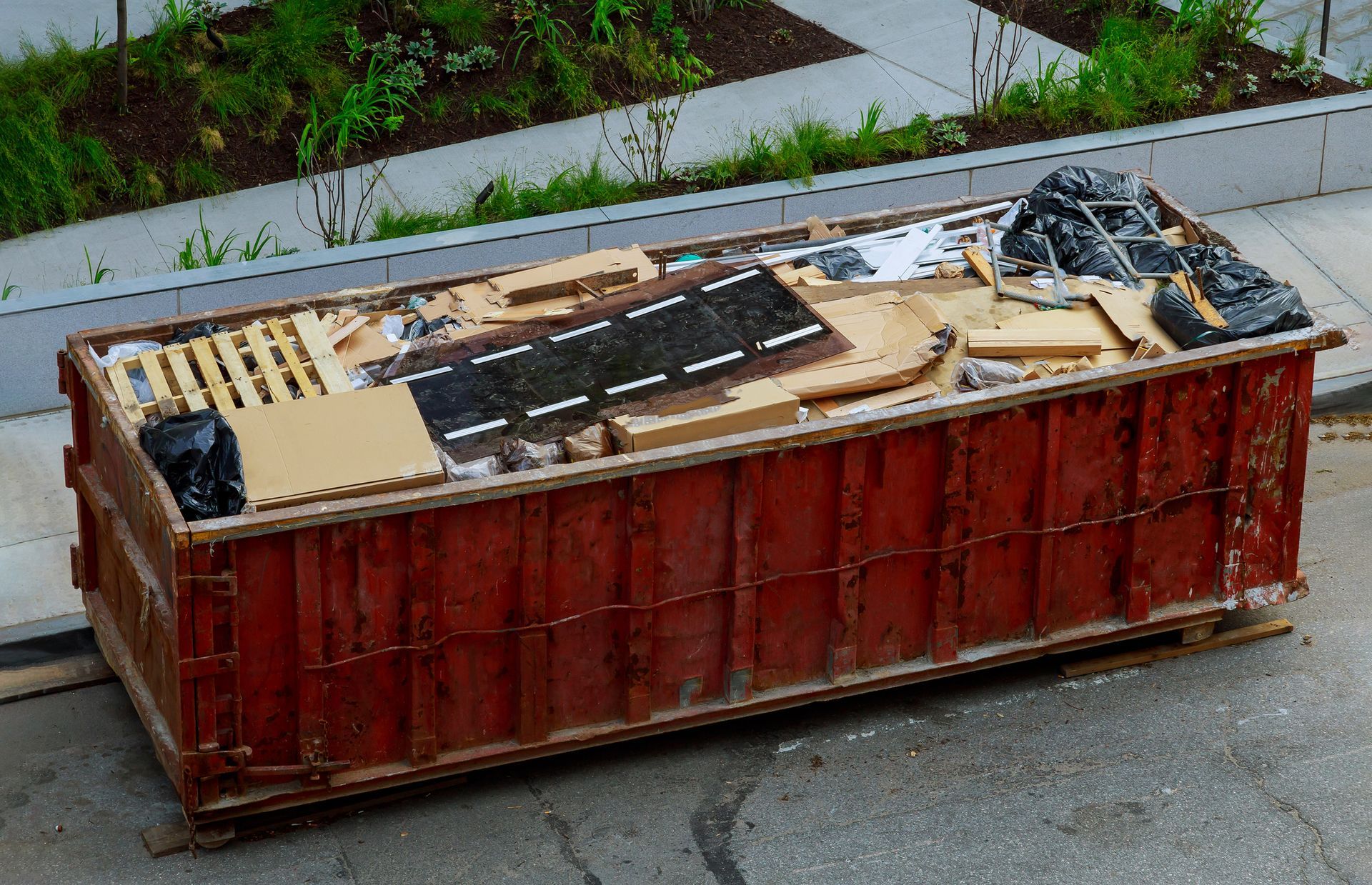 Red dumpster filled with construction debris on a city street.