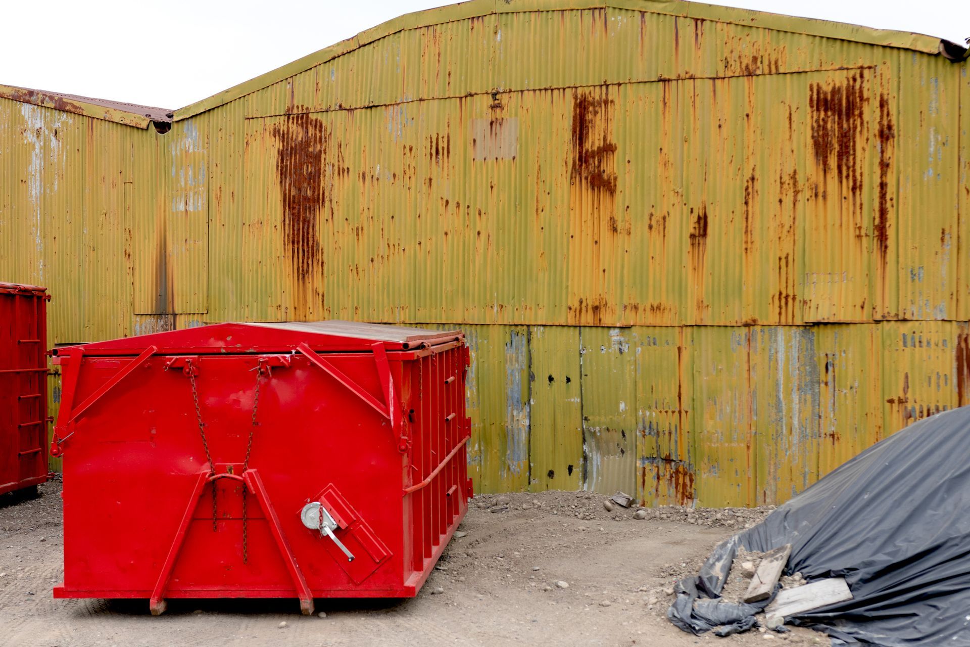 Red metal container in front of weathered, yellow corrugated metal building.