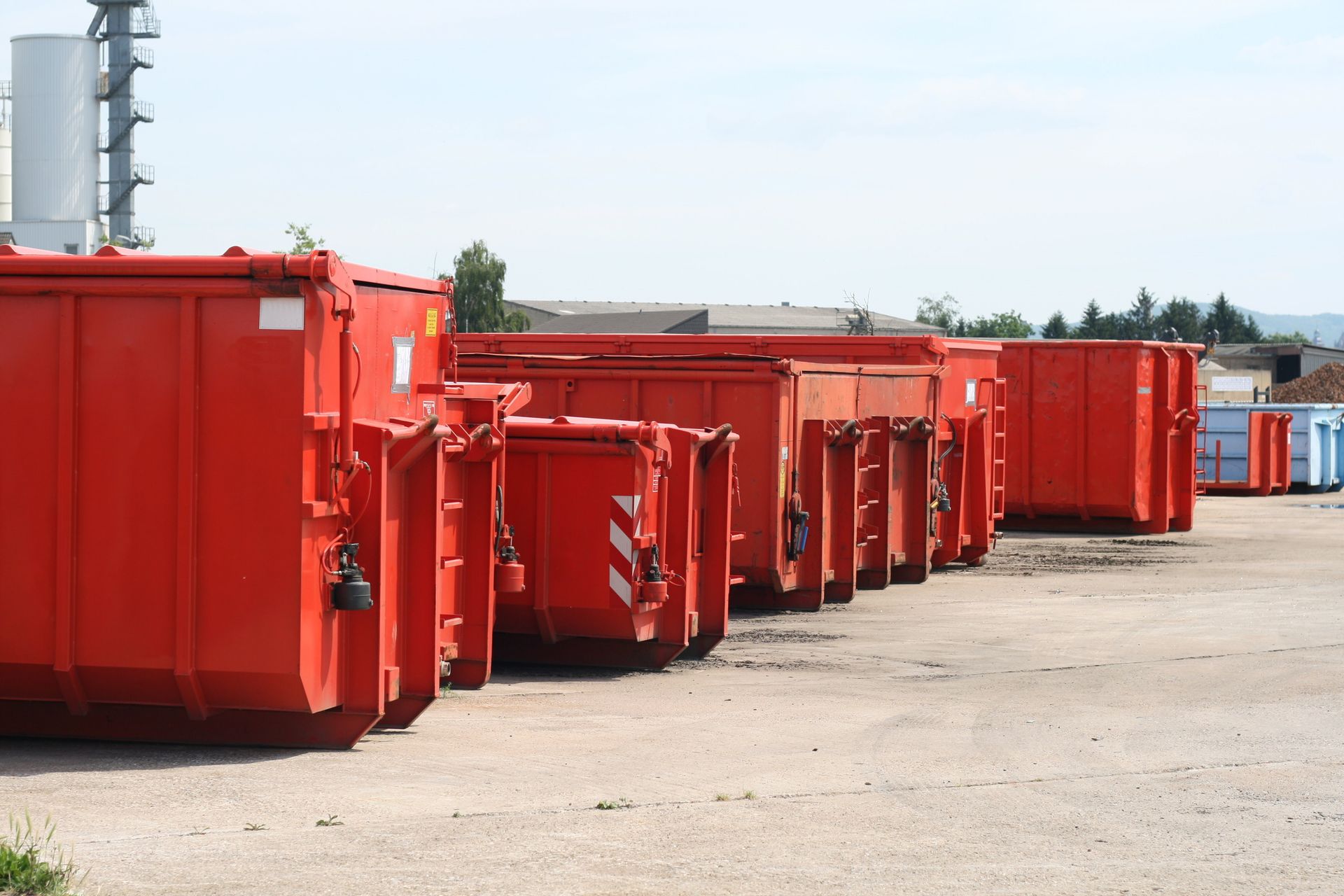 Red industrial dumpsters lined up outdoors under a blue sky.