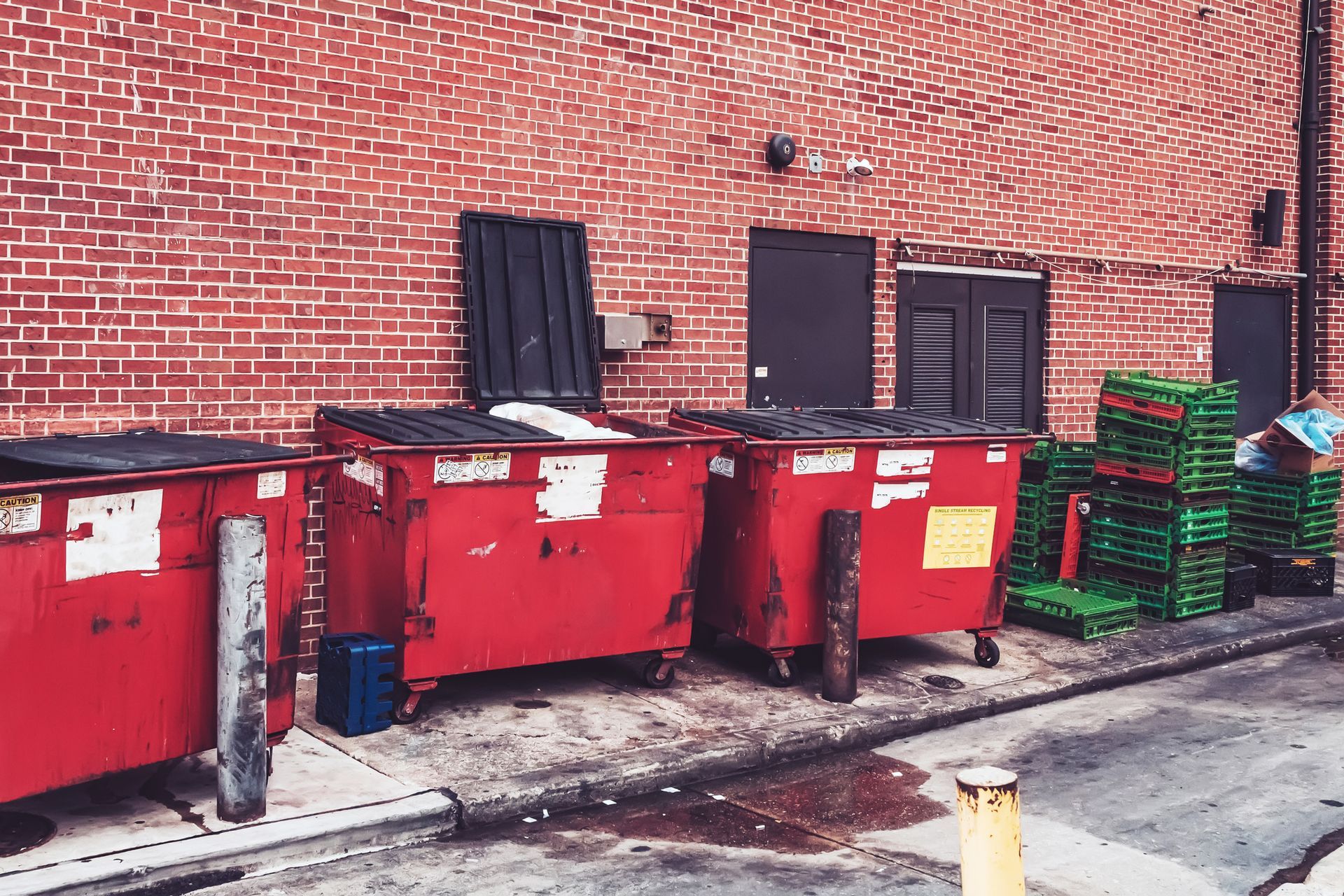 Red dumpsters next to a brick building; green pallets in the background.