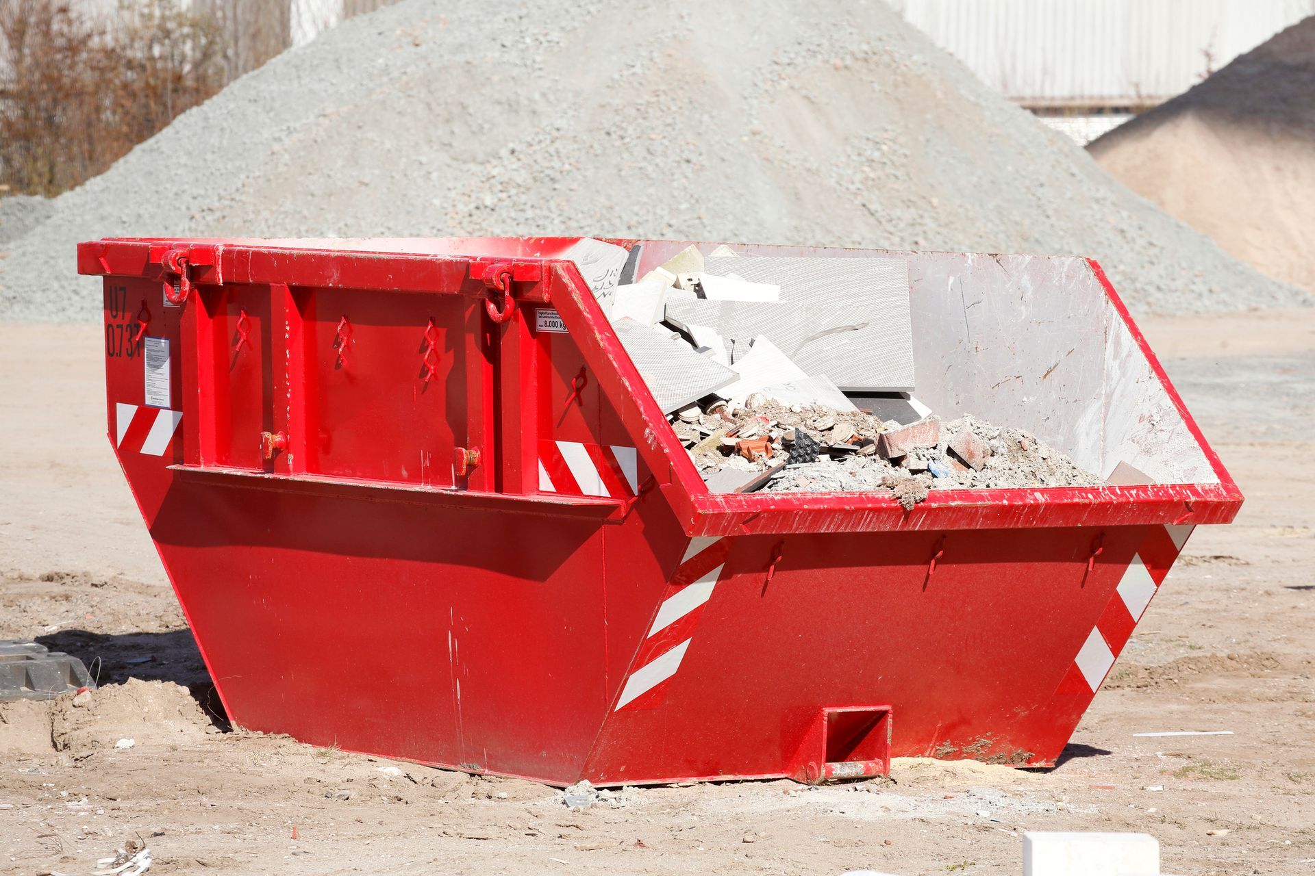 Red dumpster filled with construction debris, parked outside with a pile of gravel in the background.