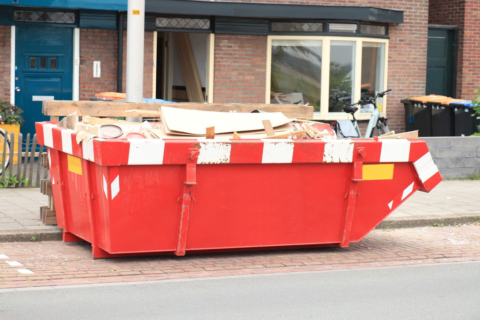 Red dumpster filled with construction debris, parked on a street in front of a house.