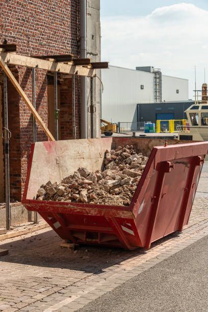 Red dumpster filled with demolition debris, outside brick building, construction site.