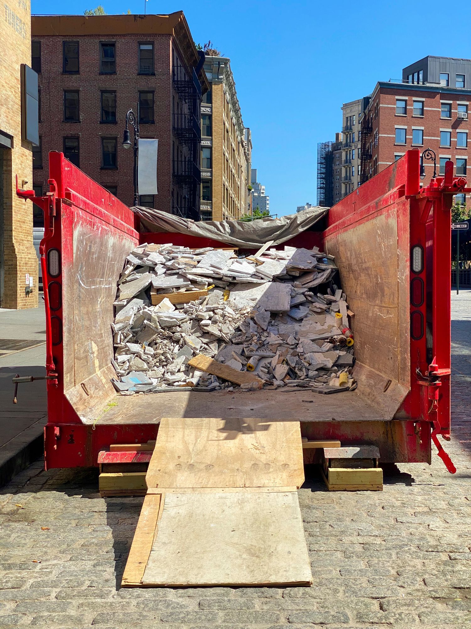 Red dumpster filled with construction debris, on a city street.