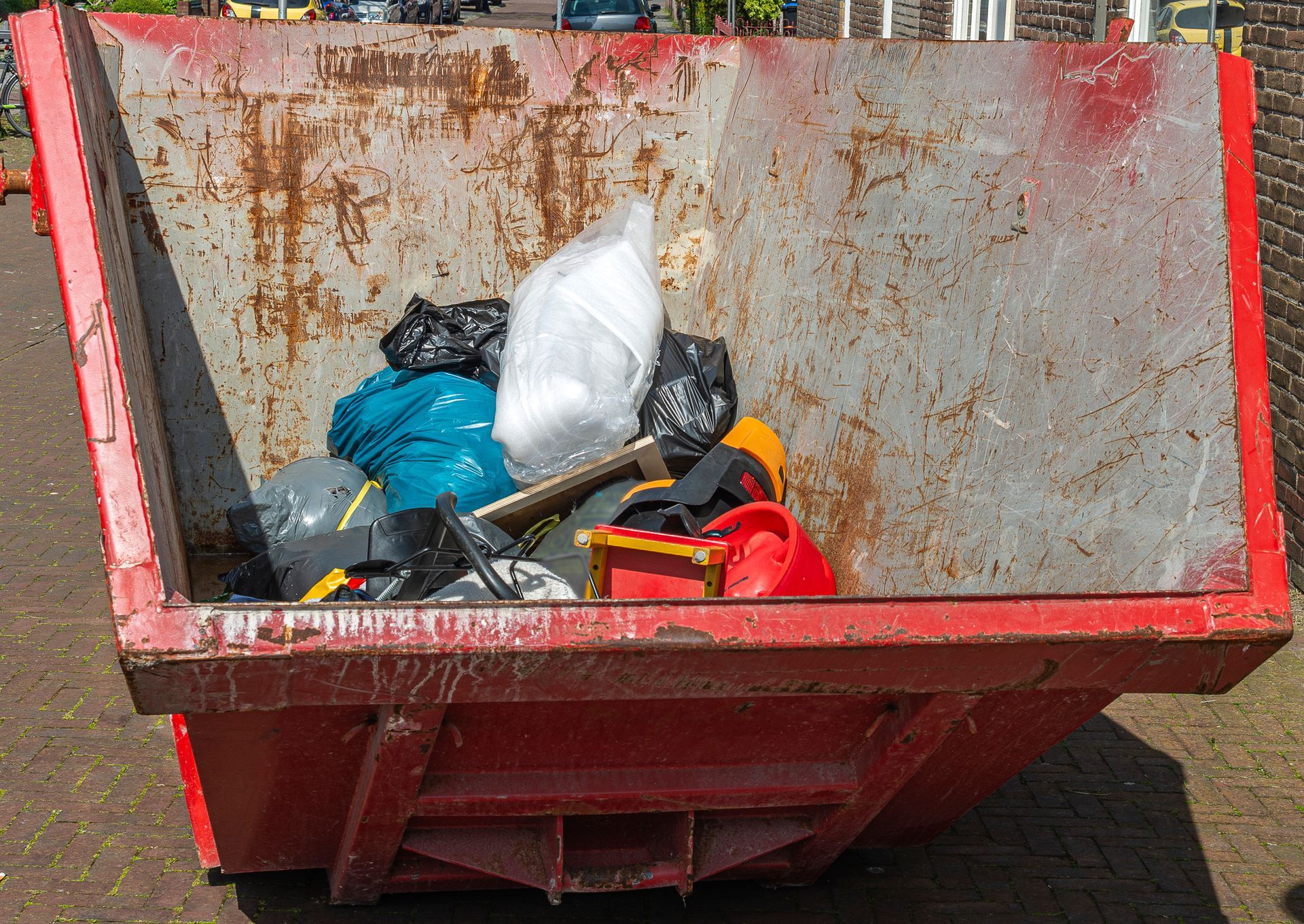 Red dumpster filled with trash bags and debris, outdoors.