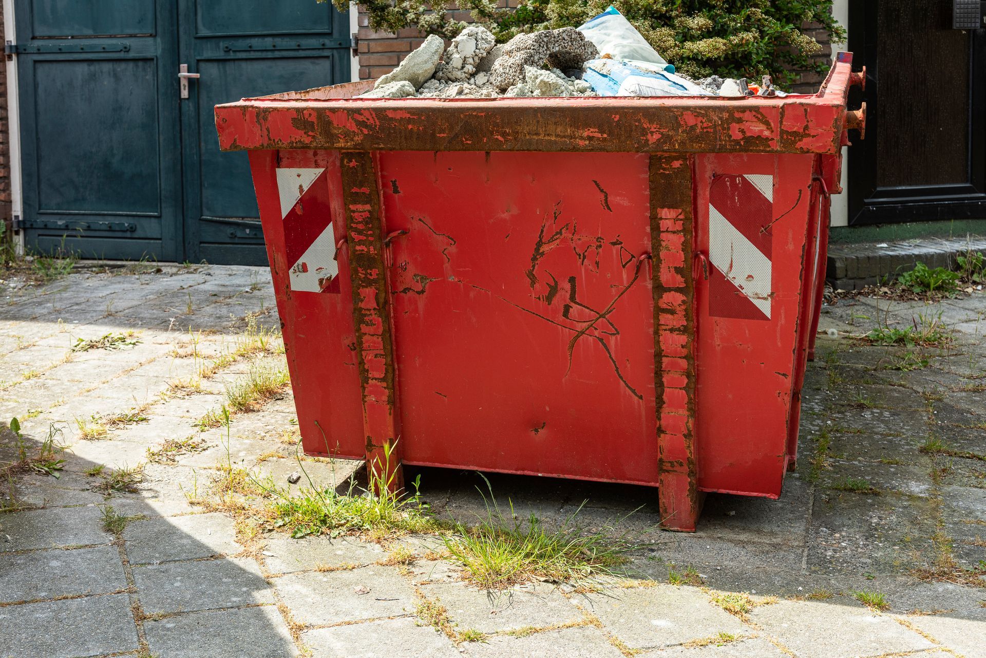 Red dumpster filled with debris, on a paved surface, against a building.