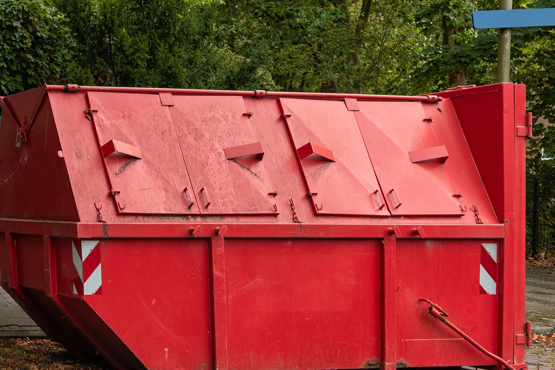 Red metal dumpster with hinged lids, outdoors.