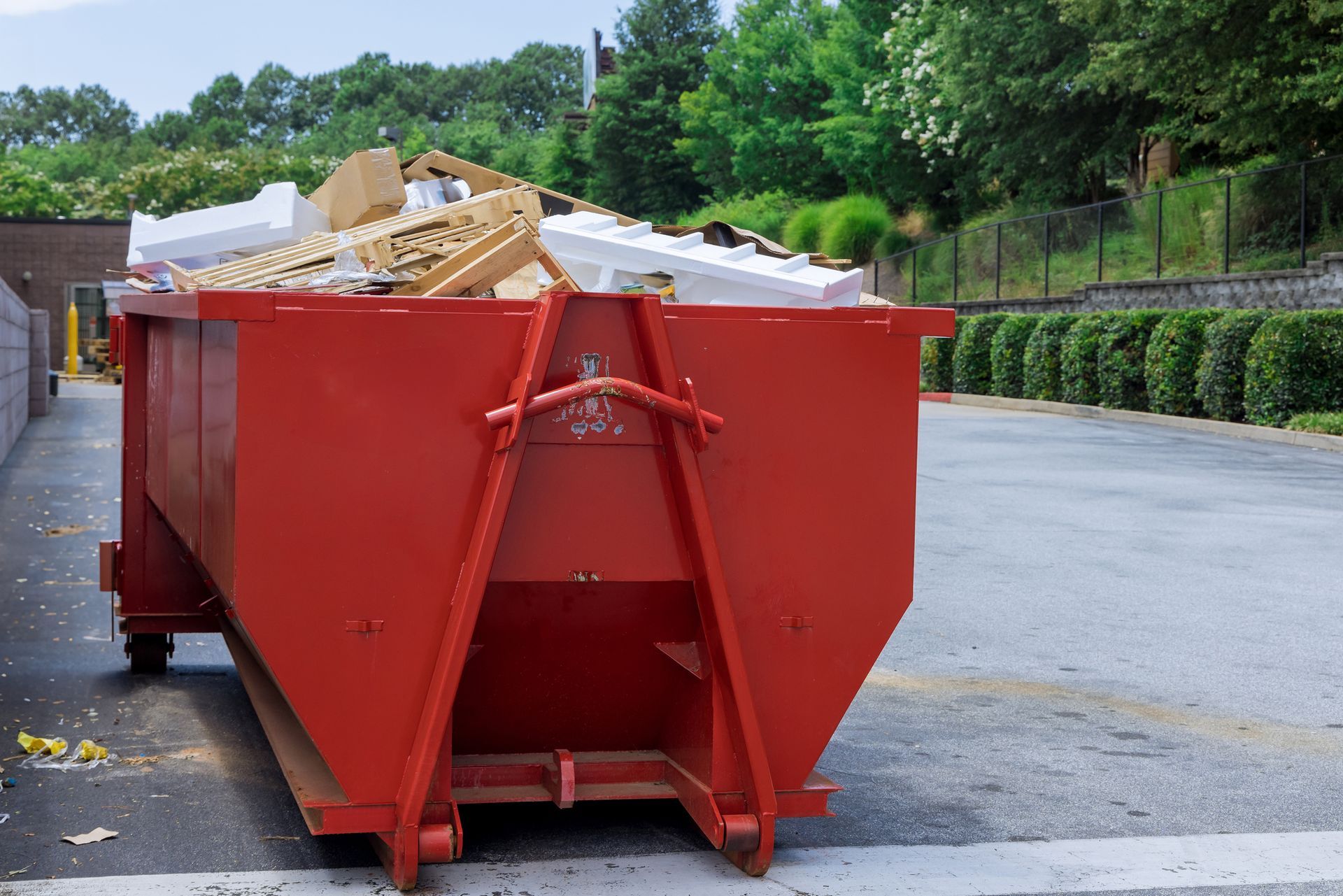 Red dumpster overflowing with construction debris, parked outside on a paved area.