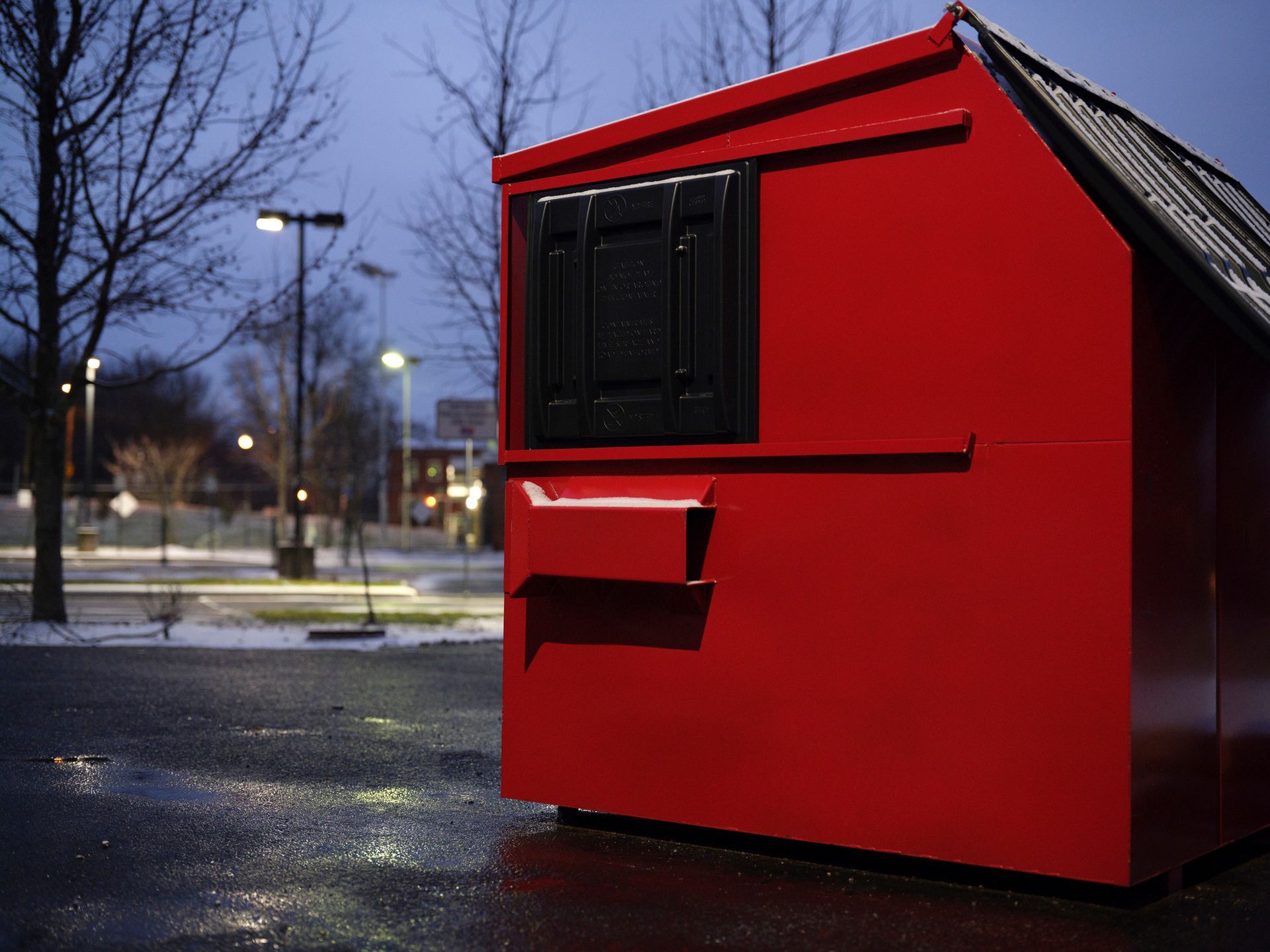Red, rectangular outdoor shelter with a window and awning, in a parking lot on a snowy day.