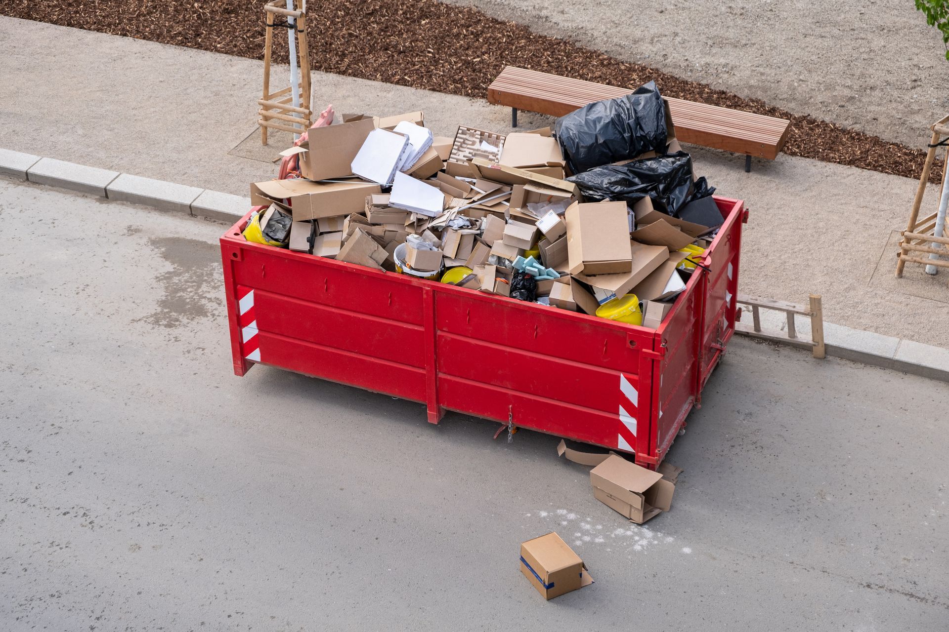 Red dumpster overflowing with cardboard boxes and trash on an asphalt surface.