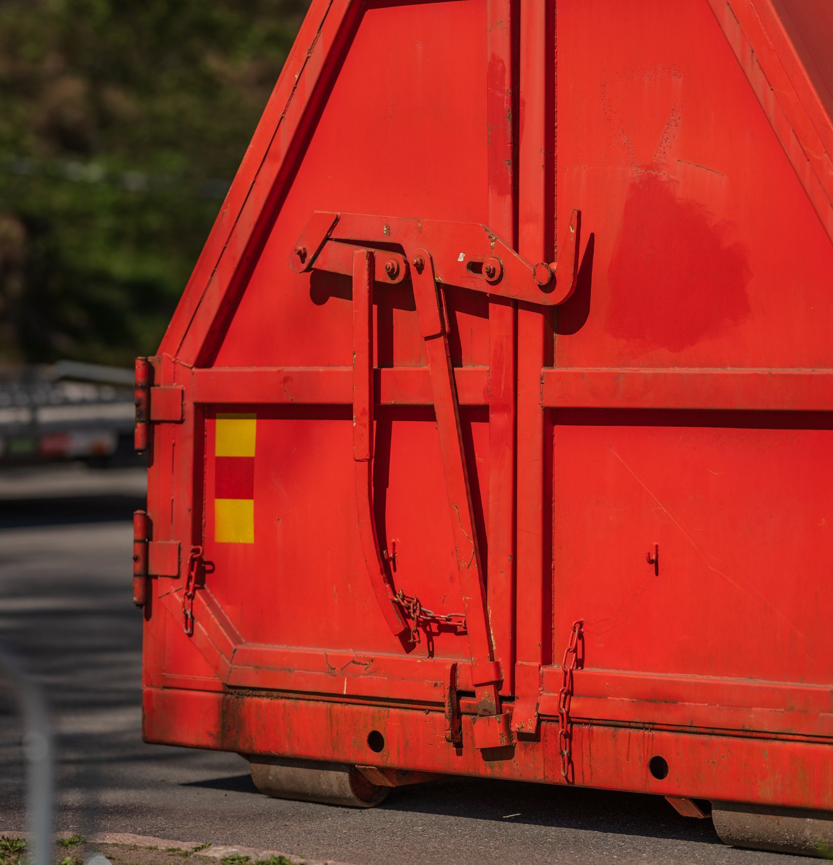 Red dumpster with metal latch detail and yellow/red safety marking.