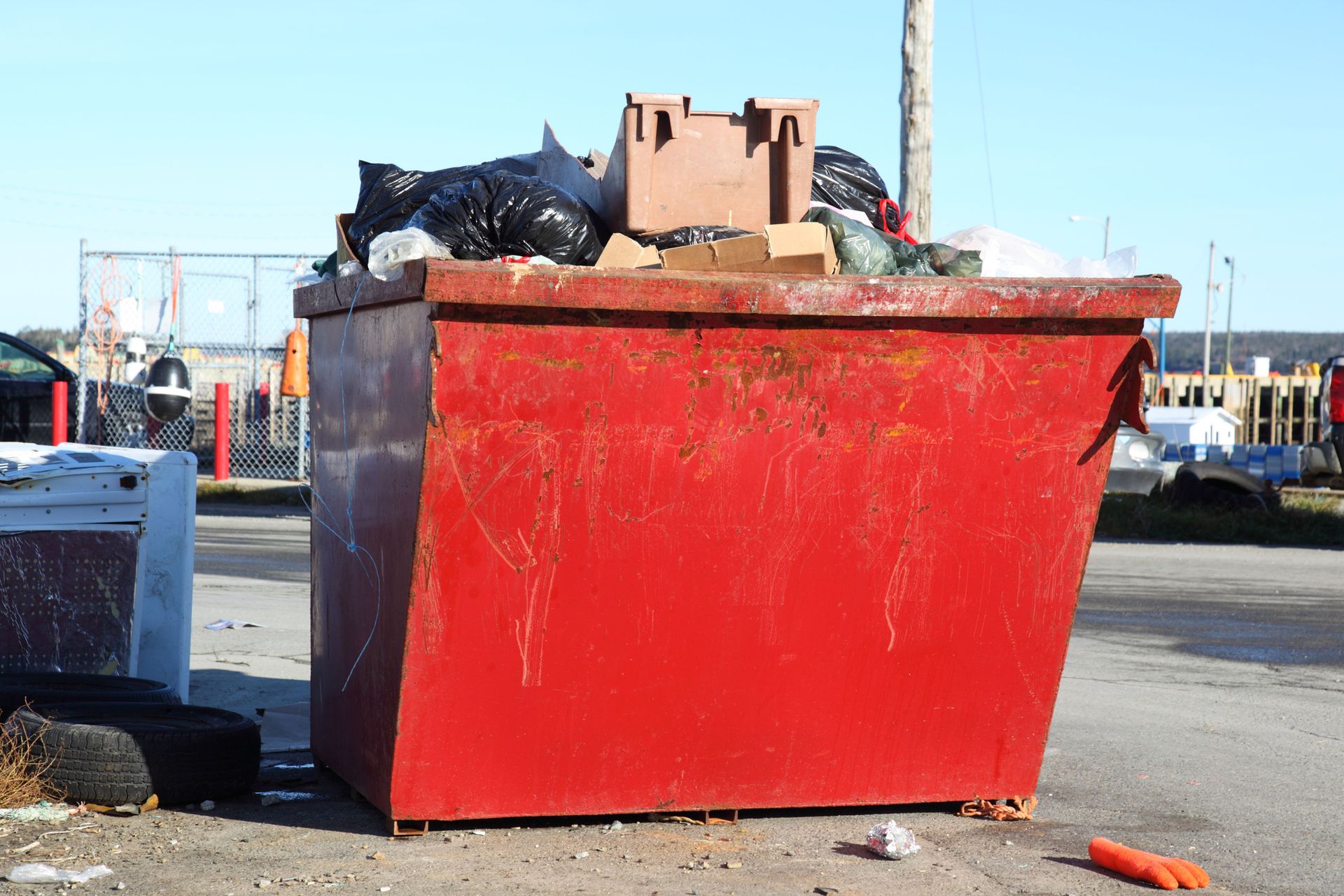 Red dumpster overflowing with trash on a sunny day.