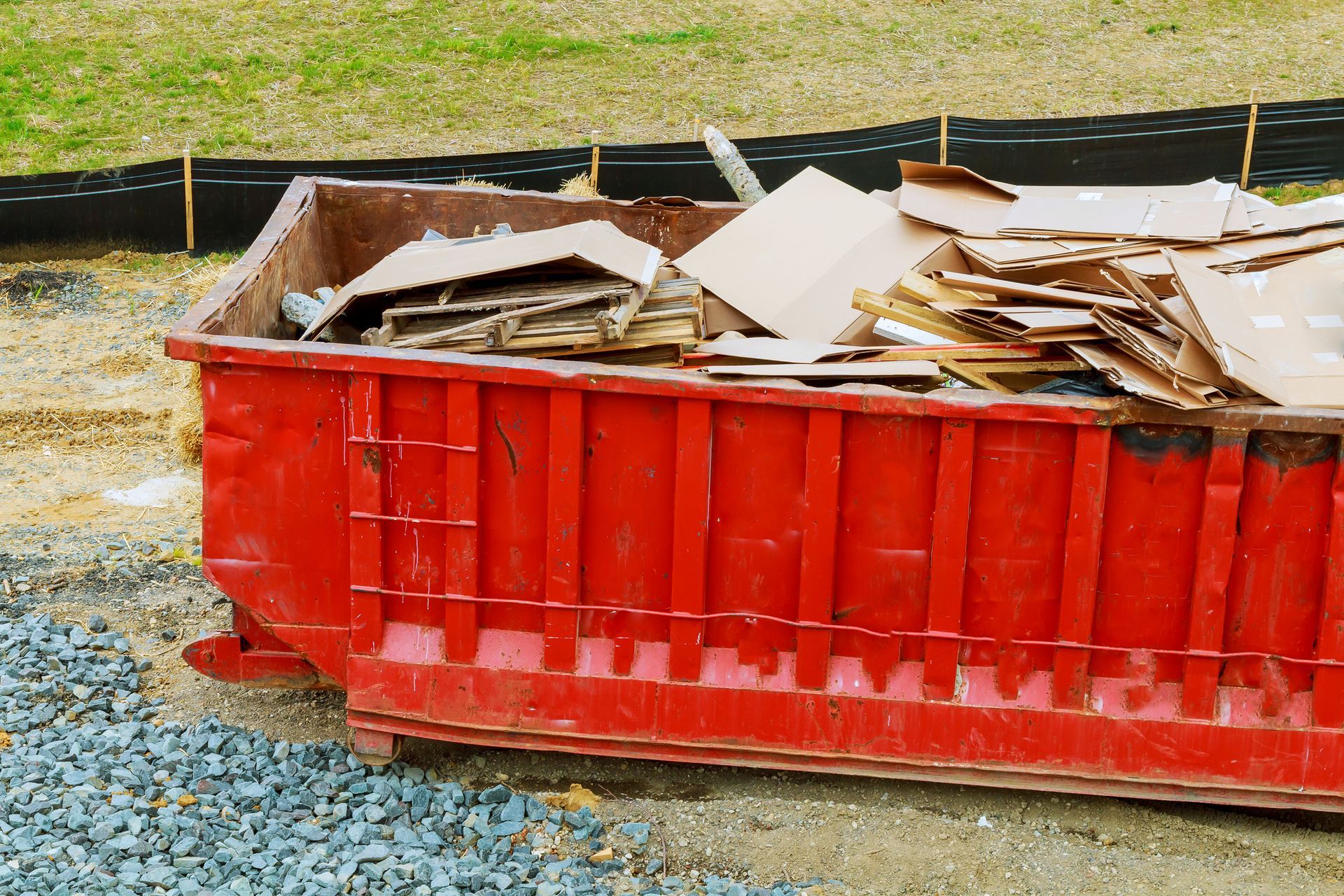Red dumpster overflowing with cardboard boxes on a construction site.