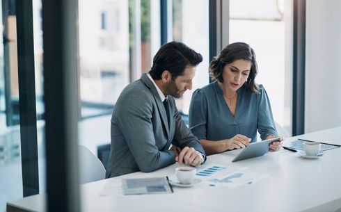 A man and a woman are sitting at a table looking at a tablet.