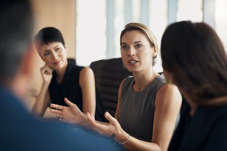 A group of women are sitting around a table talking to each other.