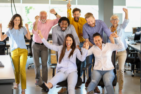 A group of people are standing in an office with their arms in the air.