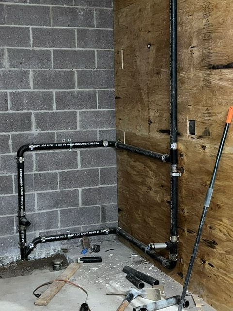 Black pipes being installed on a gray cinder block wall and a wooden wall in a room. 