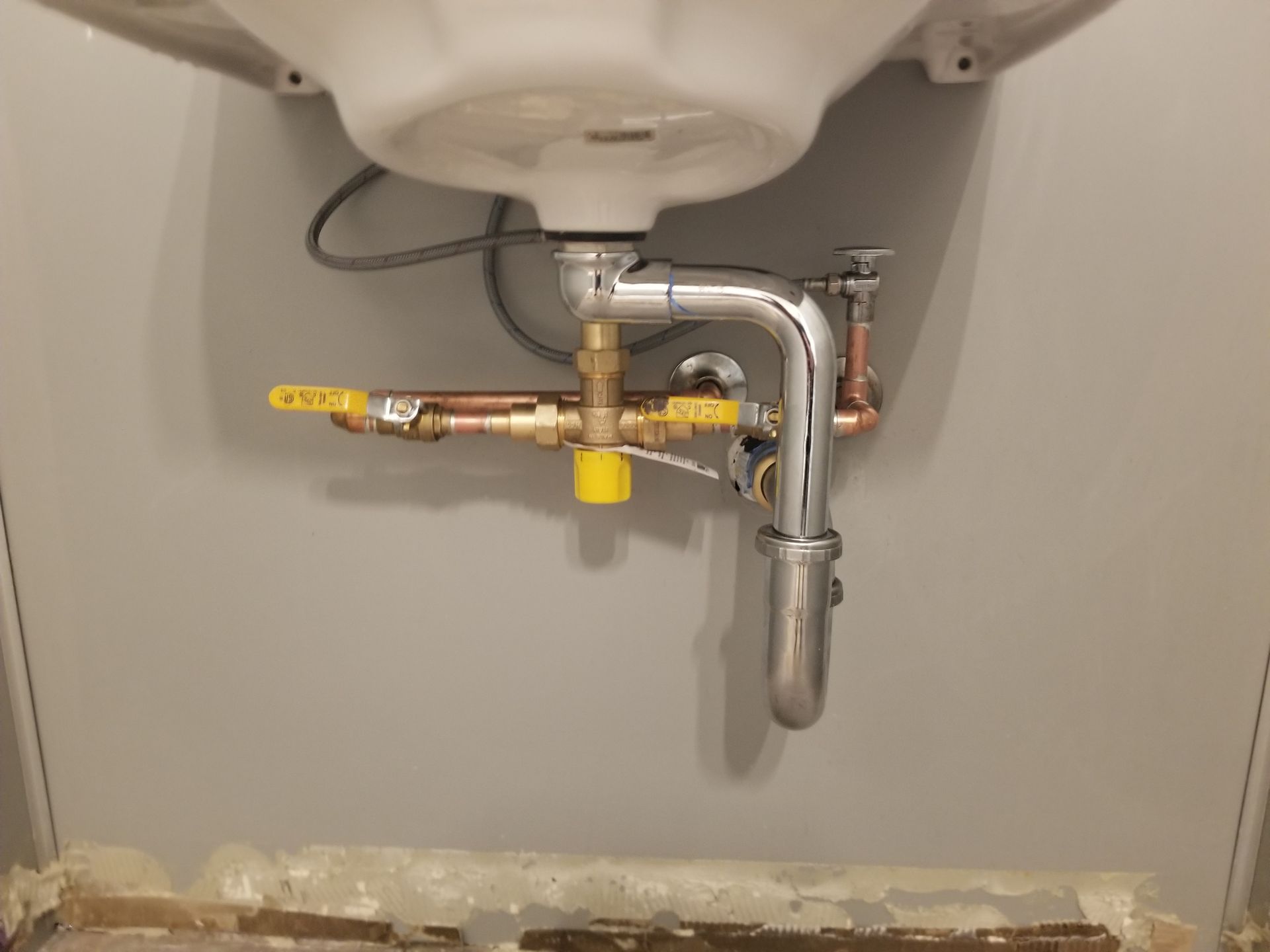 Under-sink plumbing: chrome pipes, copper tubing, and yellow shut-off valves beneath a white sink in a bathroom.