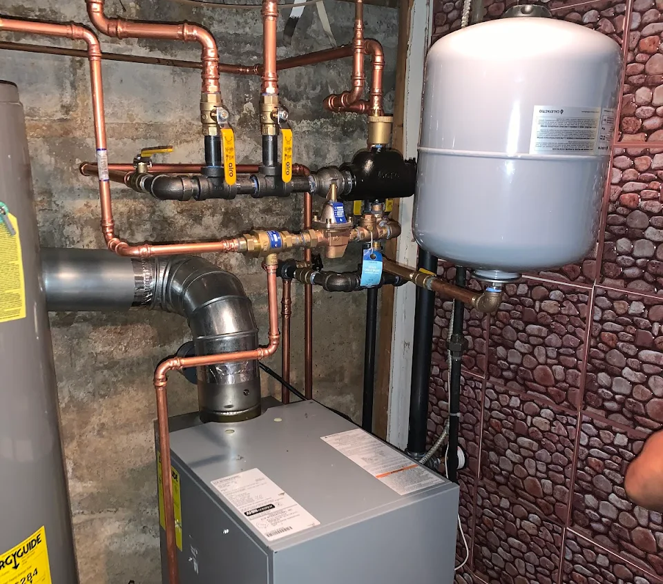 A room with a water heater and pipes on the wall.