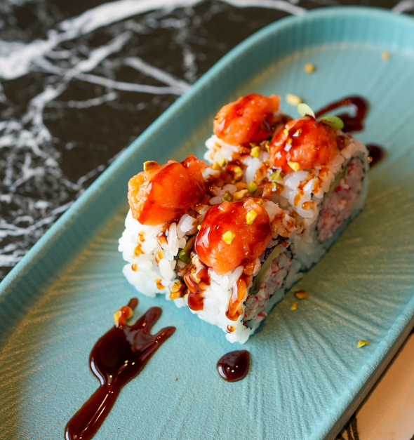 Sushi roll con salmone a cubetti e salsa, servito su un piatto color verde acqua con una spruzzata di cioccolato.