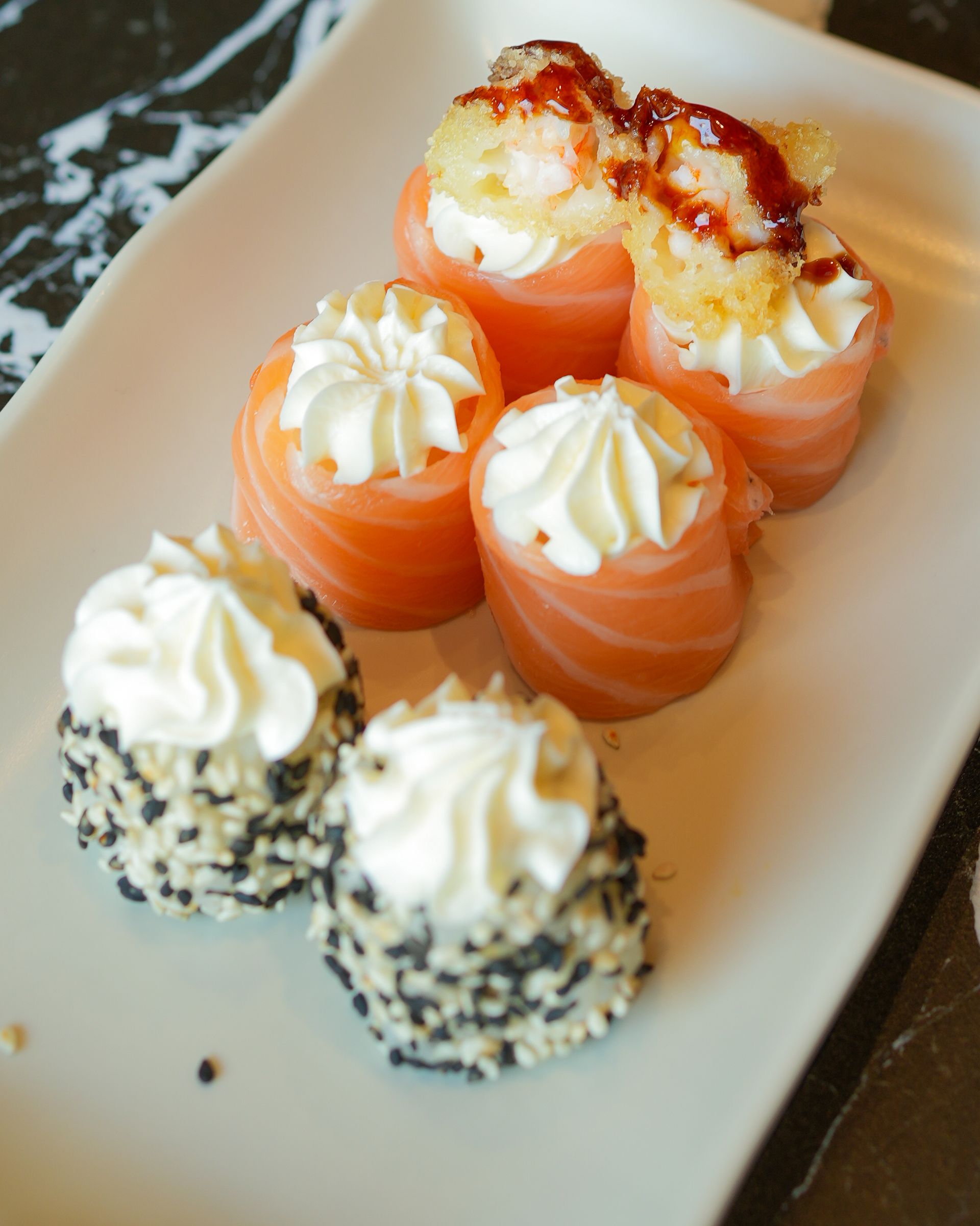 Assortimento di dessert alla crema aranciata e bianca, guarniti con panna montata e serviti su un piatto bianco.