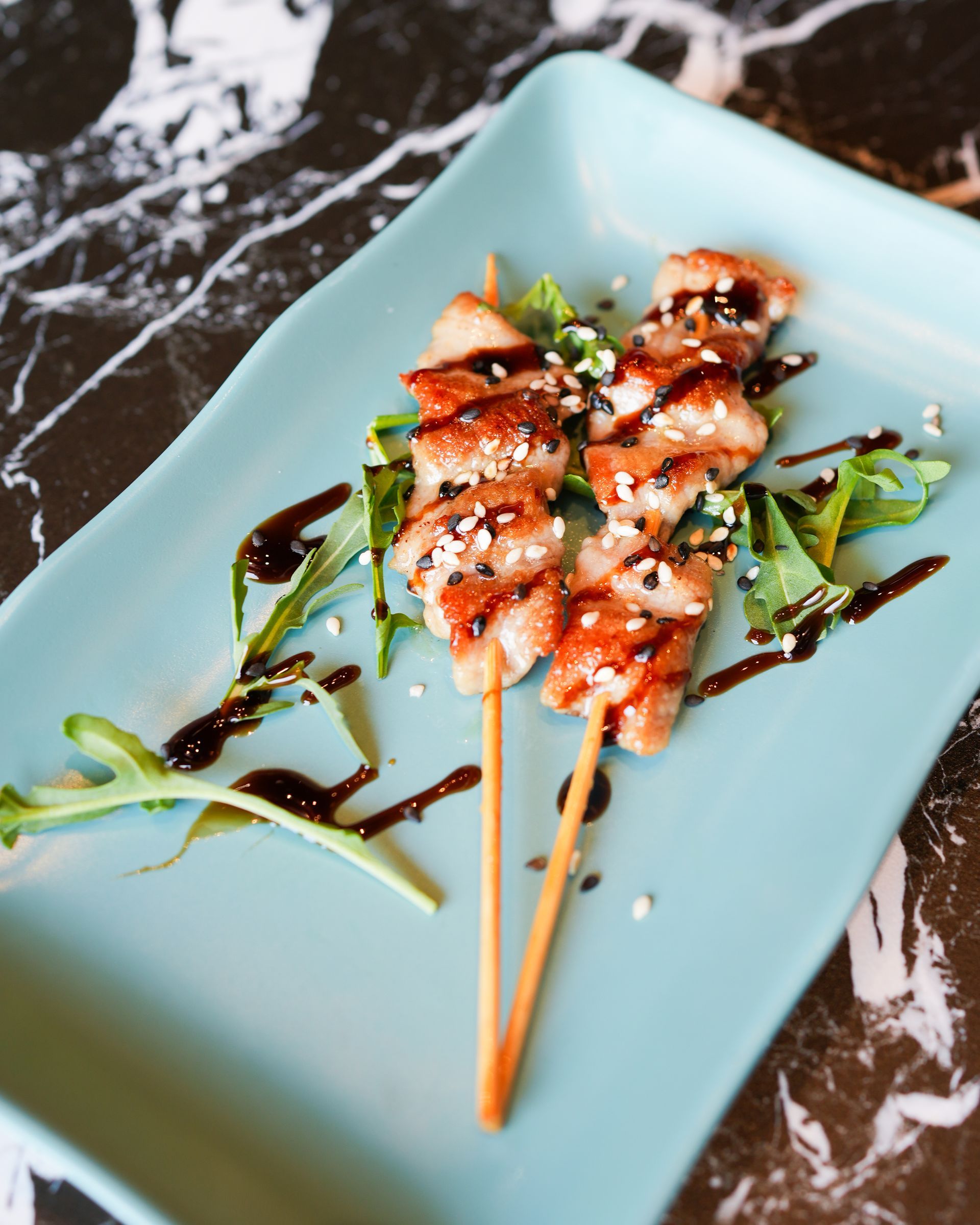 Spiedini di gamberi grigliati conditi con salsa su un piatto azzurro chiaro, guarniti con verdure.