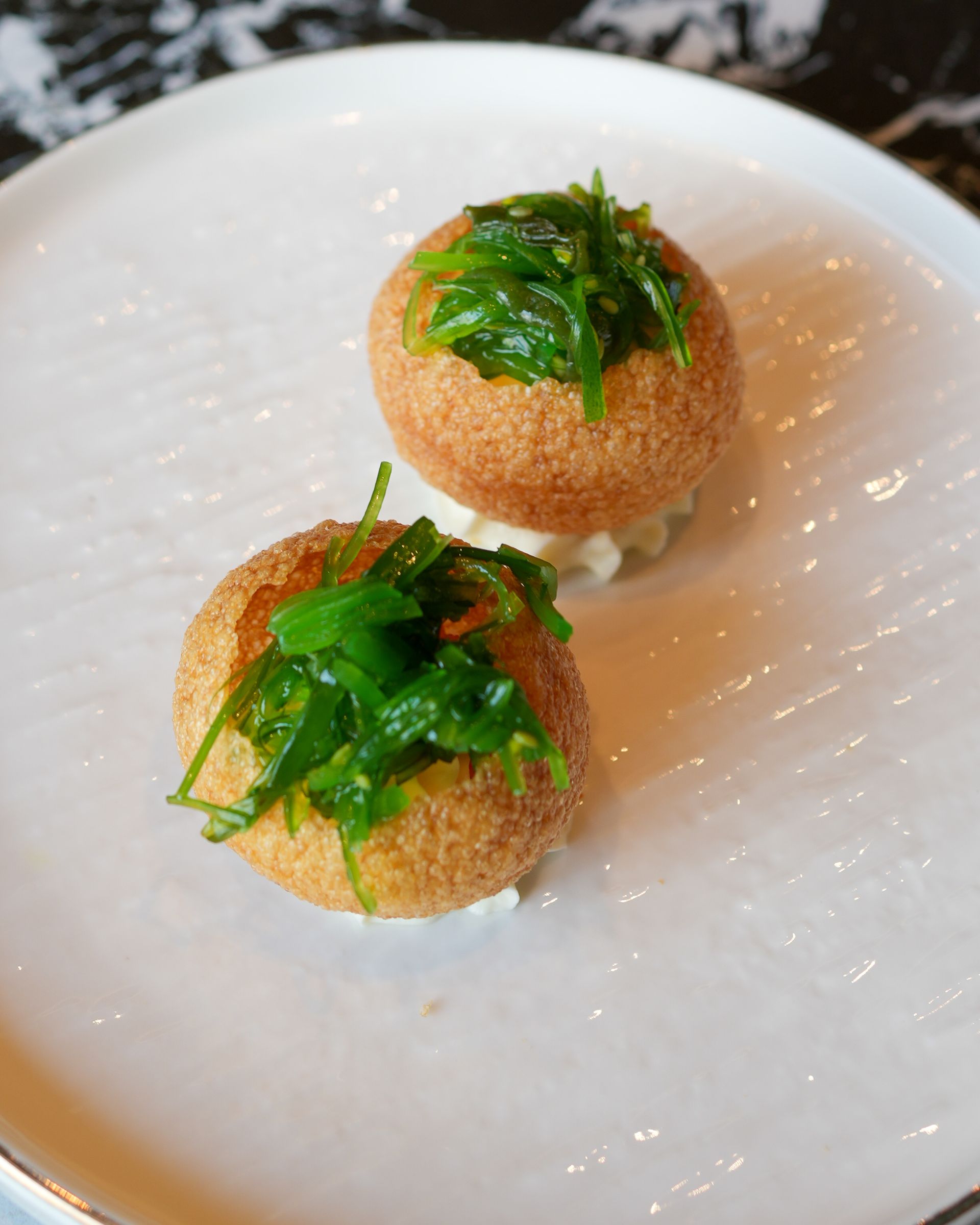 Due palline fritte da antipasto, guarnite con erbe aromatiche, servite su un piatto bianco.