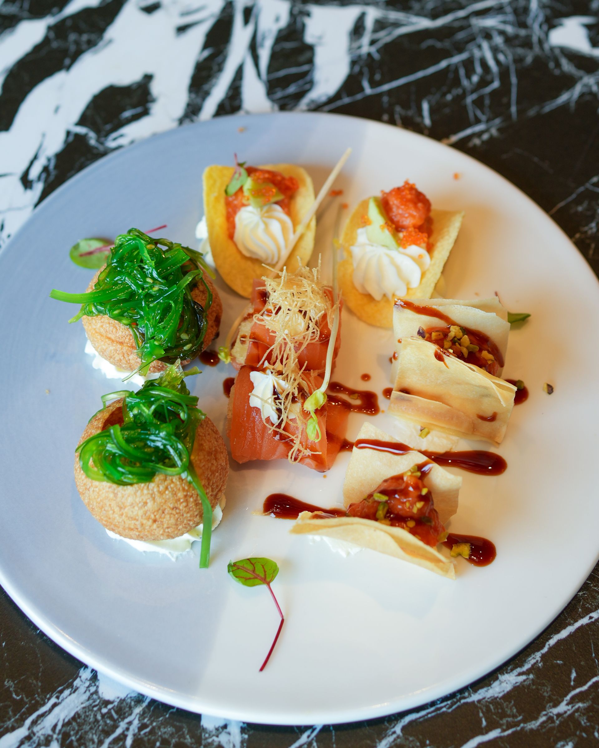 Su un tavolo scuro, un assortimento di antipasti gourmet disposti su un piatto bianco con salse colorate e microverdure.