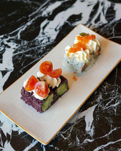Due coloratissimi bocconcini di sushi su un piatto bianco con sfondo di marmo nero.