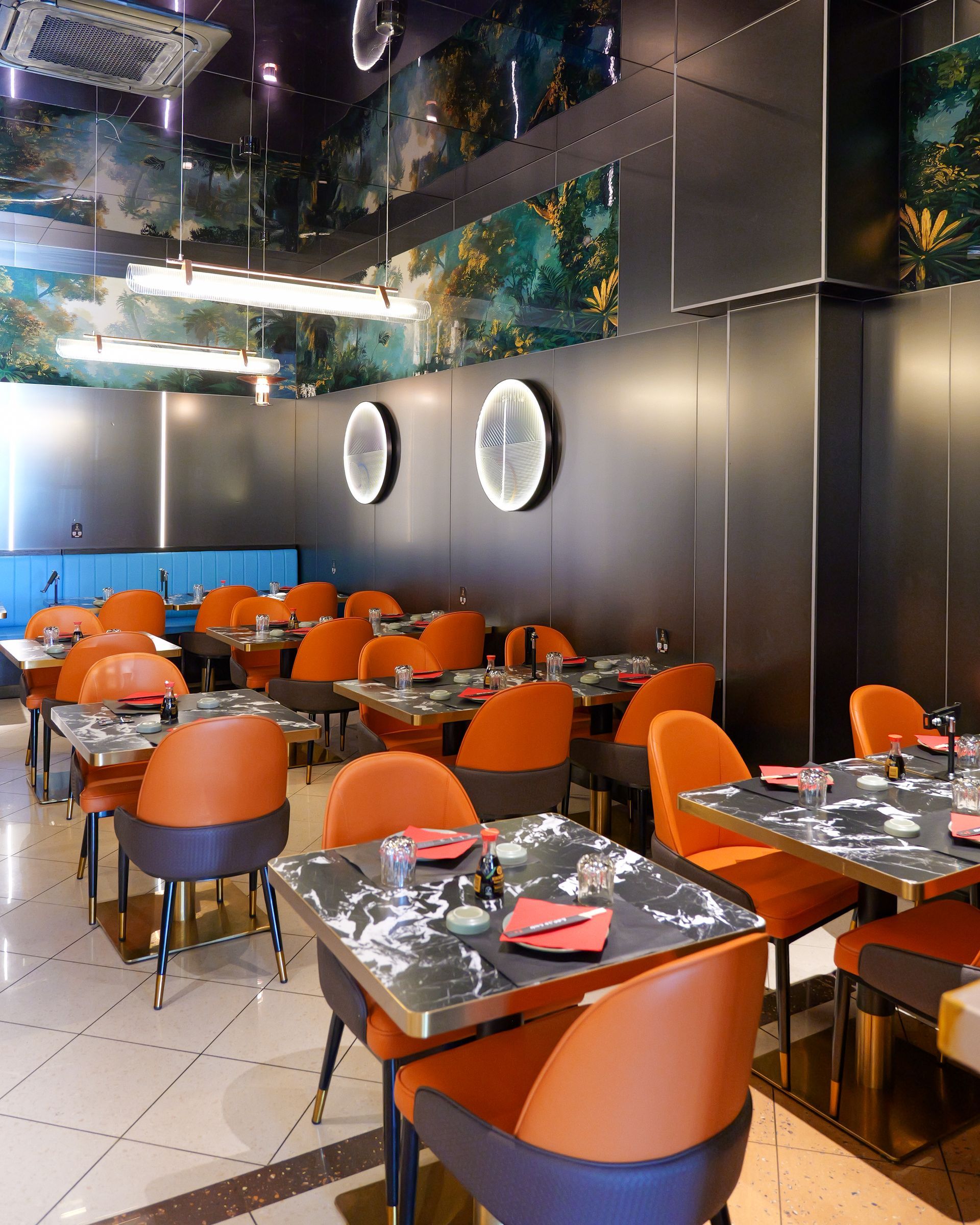 Interni moderni di un ristorante con sedie arancioni, tavoli apparecchiati, pareti nere e decorazioni murali rotonde.