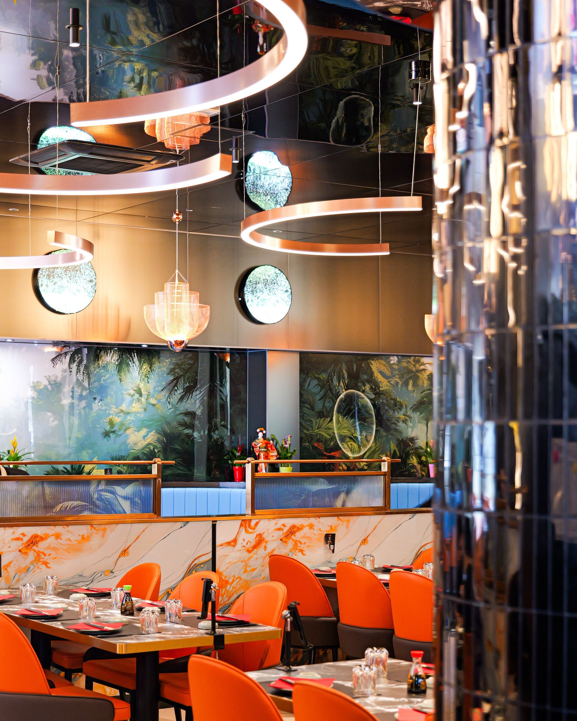 Interni moderni di un ristorante con sedie arancioni, lampade a sospensione rotonde e pareti riflettenti.