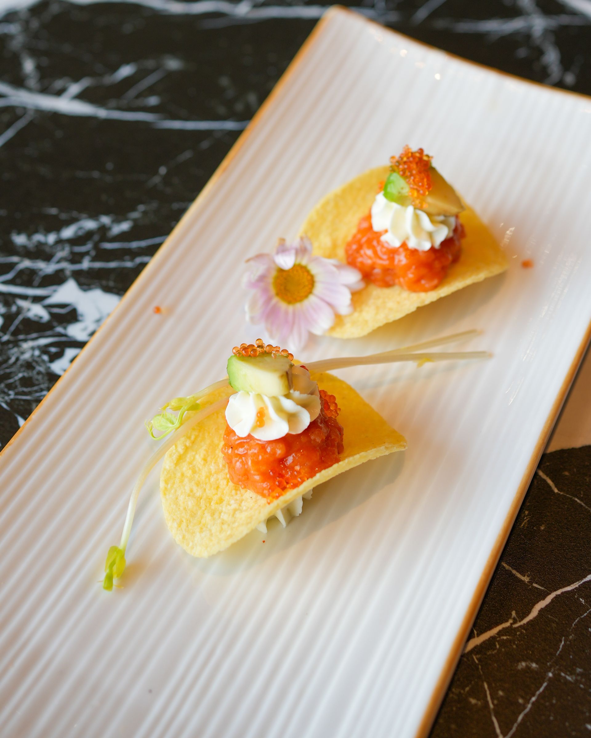 Due antipasti monoporzione con guarnizione all'arancia e decorazione floreale su un piatto da portata bianco.