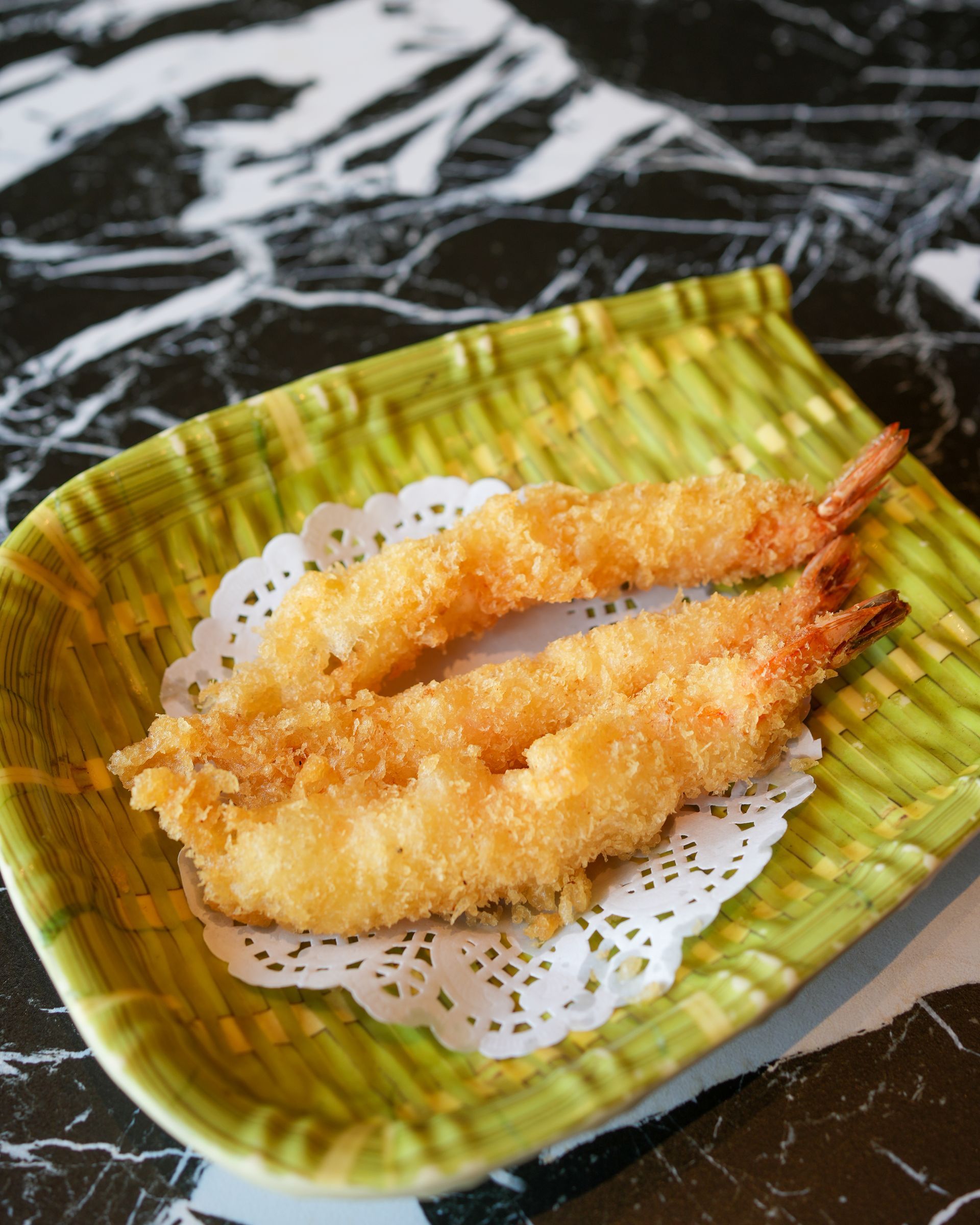 Due gamberi fritti su un piatto verde con un centrino di carta traforata.