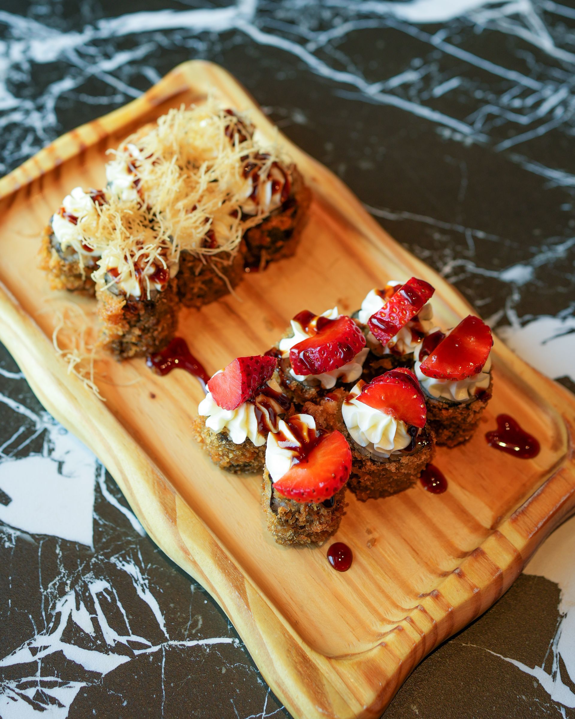 Vassoio in legno con bocconcini di dessert gourmet guarniti con fragole e salsa a filo.